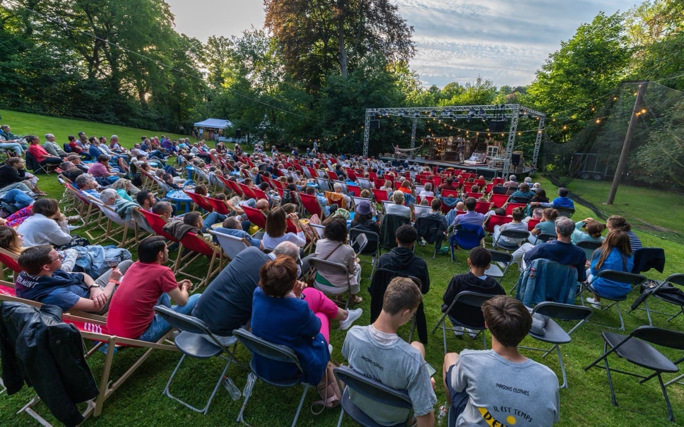 Le public installé sur la pelouse, face à la scène dans les arbres Photo Il est temps d'en rire saison été