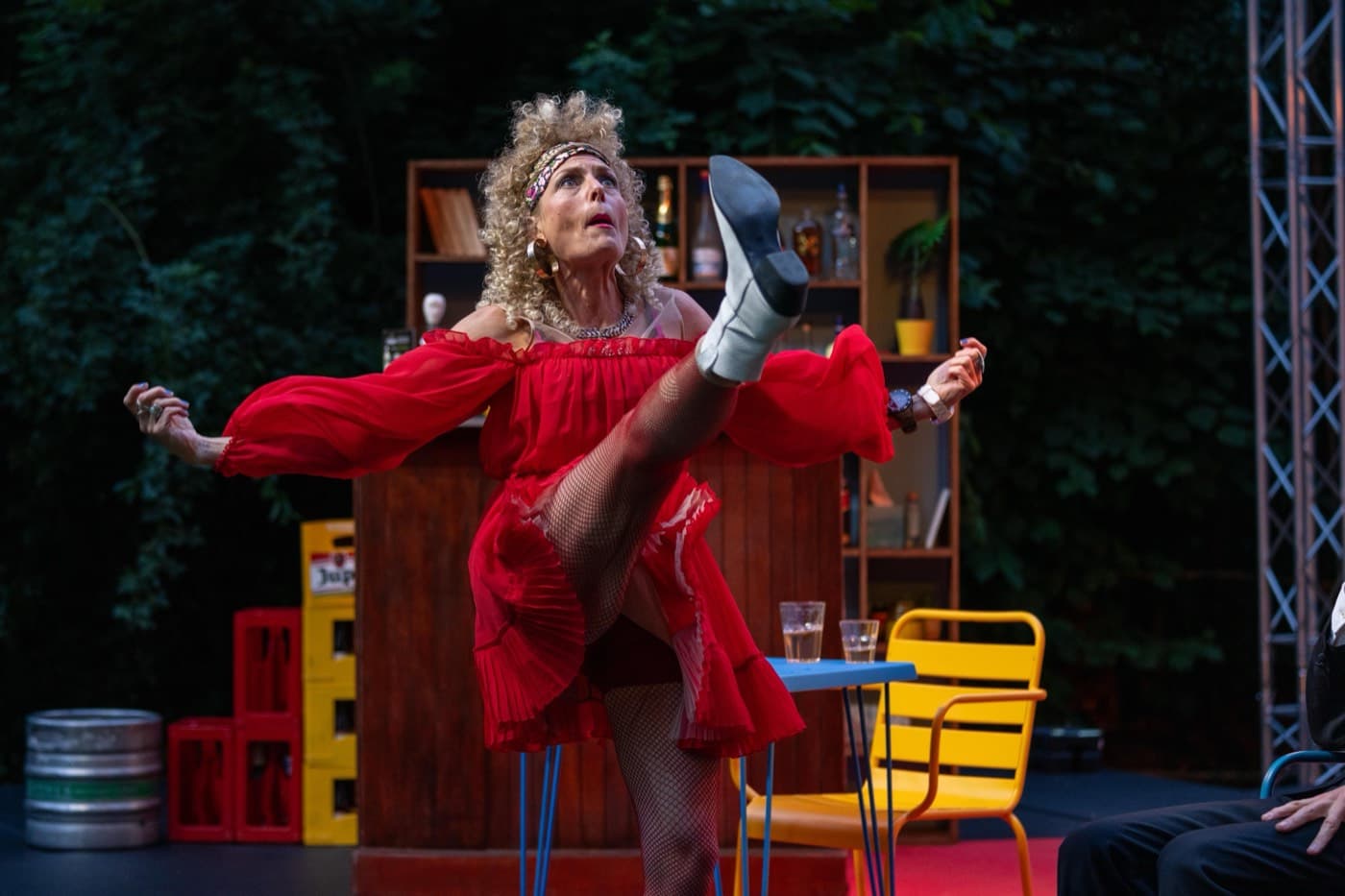 Une comédienne en robe rouge lance la jambe en l'air, sur la scène en plein air Photo Il est temps d'en rire saison été