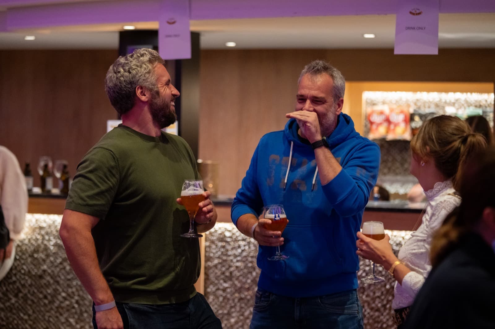 Des spectateurs rient au bar, un verre de bière à la main